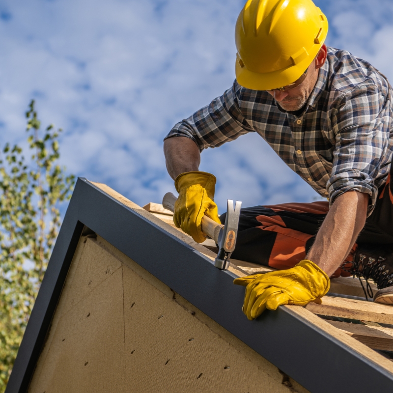 A roofer hammers a nail on a roof.